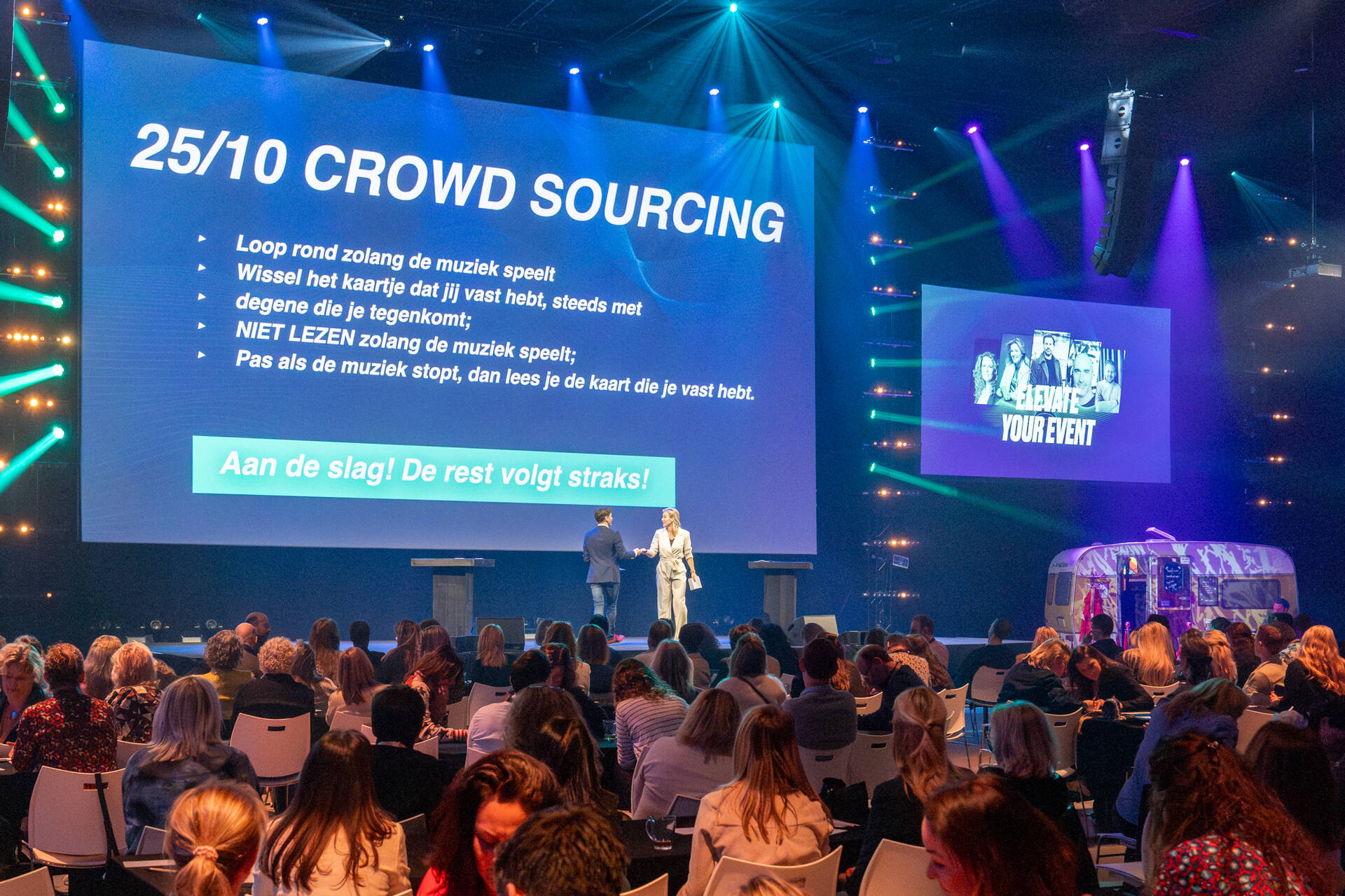 Een evenement bij de Midden Nederland Hallen met sprekers op het podium en groot publiek